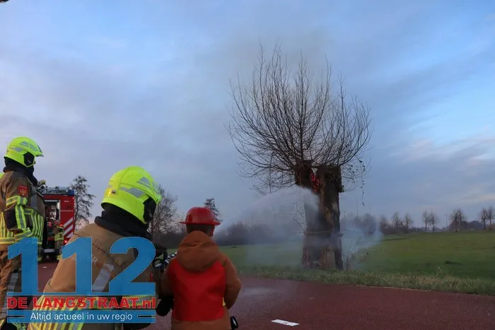 Jongentje in brandweerkleding helpt brandweer bij blussen brandende knotwilg Sprang-Capelle 112 De Langstraat